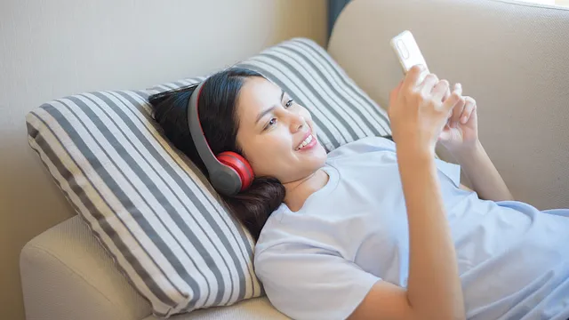 woman listening to audio on headphones while using smartphone
